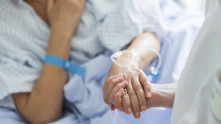 Paziente in ospedale con flebo al braccio viene rassicurato dalla stretta di mano di un medico, concetto di assistenza sanitaria.