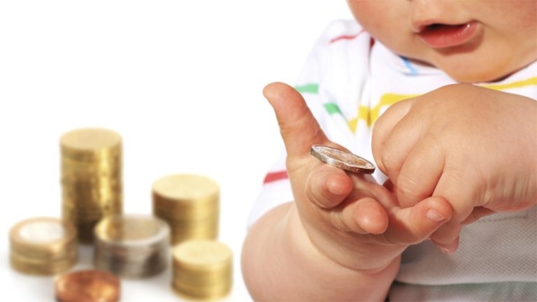 Bambino che tiene una moneta in mano con pile di monete sfocate sullo sfondo, concetto di risparmio e finanza per bambini.