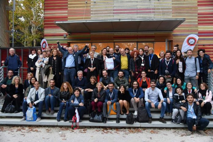 Gruppo numeroso di persone sorridenti su una scalinata all’aperto davanti a un edificio moderno, durante un evento o incontro.