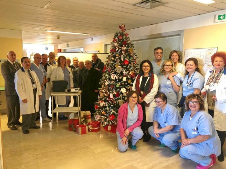 Personale medico e infermieristico riunito attorno a un albero di Natale decorato in ospedale, atmosfera festiva e professionale.