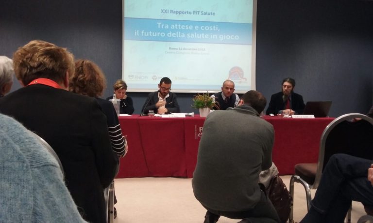 Conferenza sulla salute con relatori seduti a un tavolo davanti a una platea e slide proiettata sul rapporto PIT Salute.