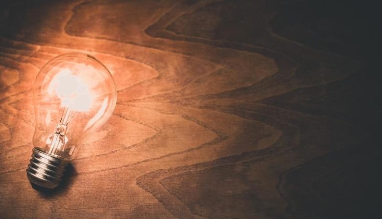 Lampadina accesa su superficie di legno con luce calda, simbolo di idee e creatività.